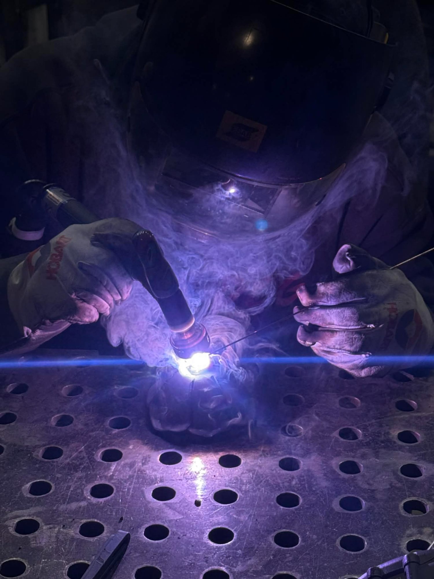 Close-up TIG welding on perforated steel plate — custom metal work